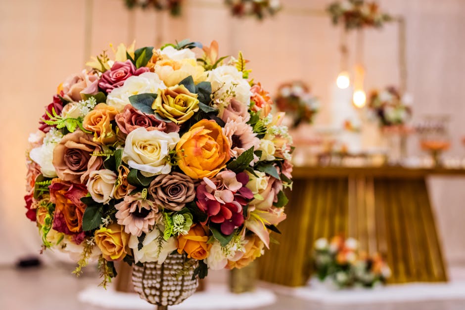 A close-up of a large, round floral bouquet featuring a variety of fresh roses, peonies, and hydrangeas in shades of pink, cream, peach, and yellow, arranged with green foliage. The bouquet is wrapped