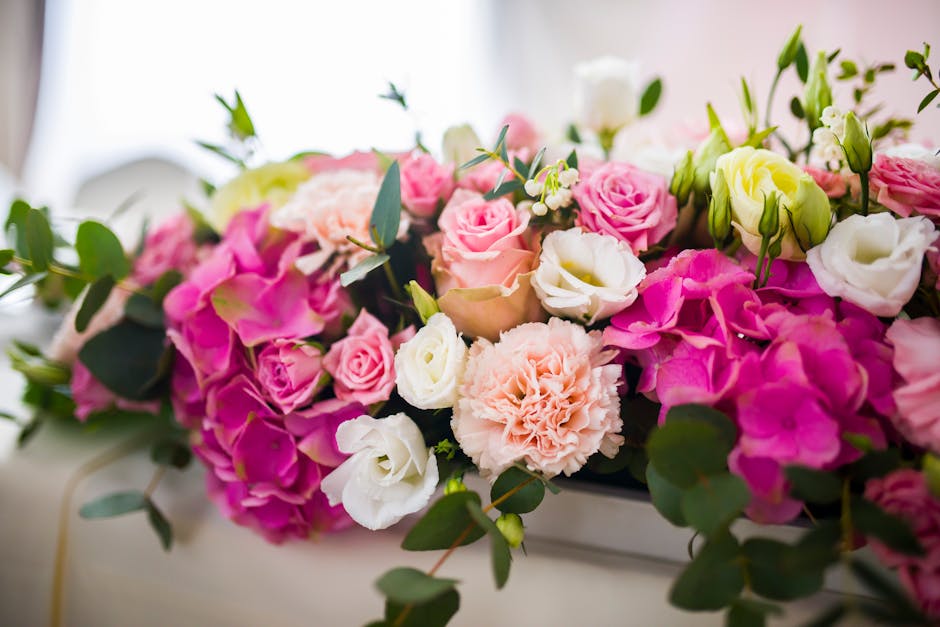 A close-up view of a floral arrangement featuring pink and white roses, pale peach carnations, hydrangeas, and lisianthus, complemented by sprigs of eucalyptus and other greenery. The flowers are fres