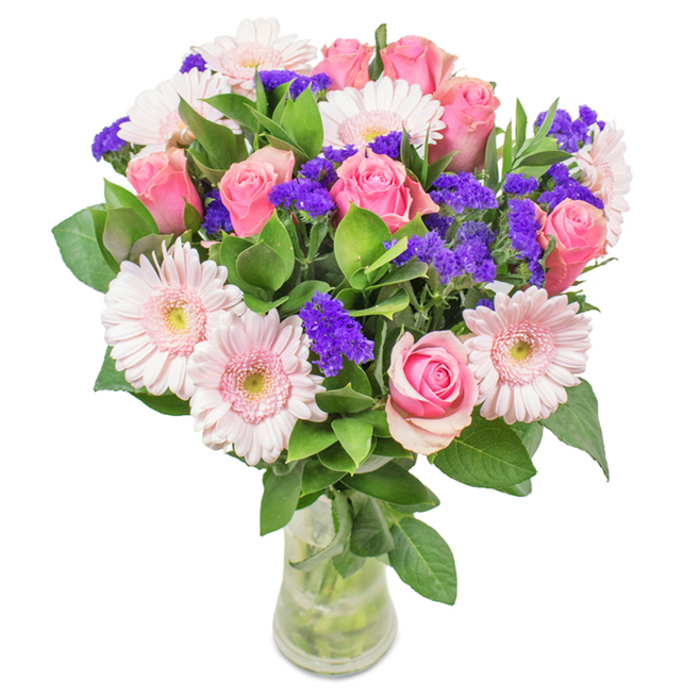 Showcased in a clear glass vase, this floral arrangement is a vibrant blend of South Hornchurch's signature style and botanical charm. Approximately seven to nine medium pink roses-some petals tightly curled and others beginning to bloom-establish a romantic centerpiece, their form reminiscent of the classic English garden roses often seen in Rainham Hall's historic grounds. These are beautifully paired with five to seven pale pink Gerbera daisies, their large, round faces and light centers capturing the delicate pinks of a spring sunrise over Harrow Lodge. Interspersed flashes of statice in vivid purple offer brilliant textural contrast, echoing the exuberant wildflowers blooming along the Ingrebourne Valley. The bouquet's lush, deep green foliage forms a robust base, enhancing both volume and freshness, while the vase's clear sides reveal the water and intricate stems below. Suitable for all occasions-birthdays, anniversaries, or as an elegant addition to a South Hornchurch home-this carefully crafted bouquet embodies the community's warmth and generosity, sending joy and heartfelt celebration with every delivery.